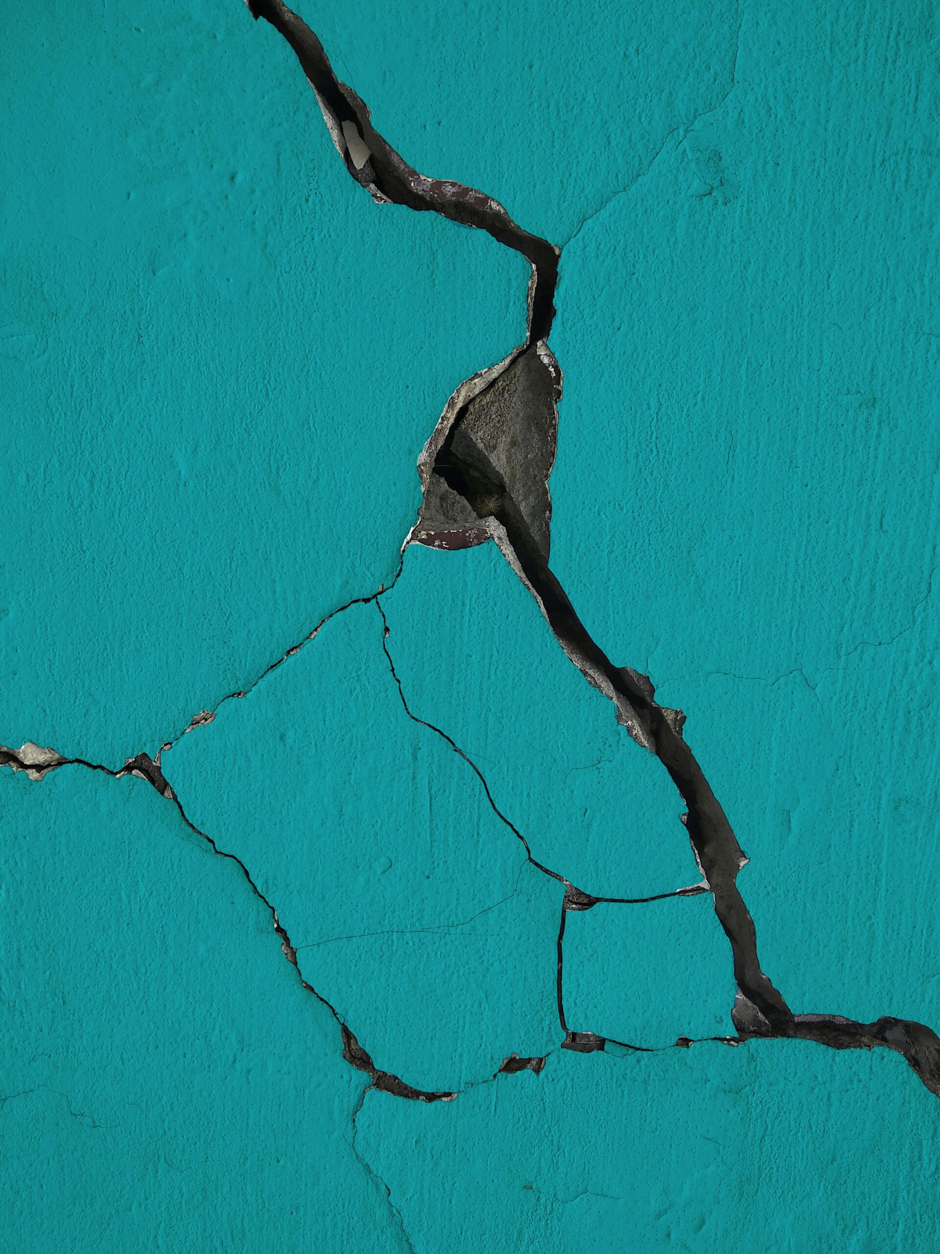 Close-up of cracked turquoise wall texture showing structural damage and peeling paint.